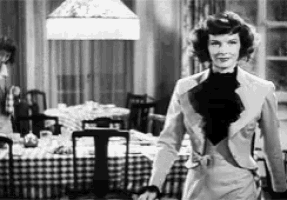 a black and white photo of a woman standing in a dining room