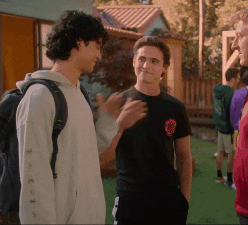 a man wearing a black t-shirt with a circle on it talks to another man wearing a white sweatshirt