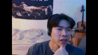 a man is making a funny face in front of a guitar and a poster of a man laying on a bed .