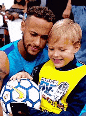 a man holding a soccer ball next to a young boy wearing a shirt that says neymar