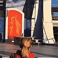 a woman in a red shirt is sitting in front of a building with a large red sign on it