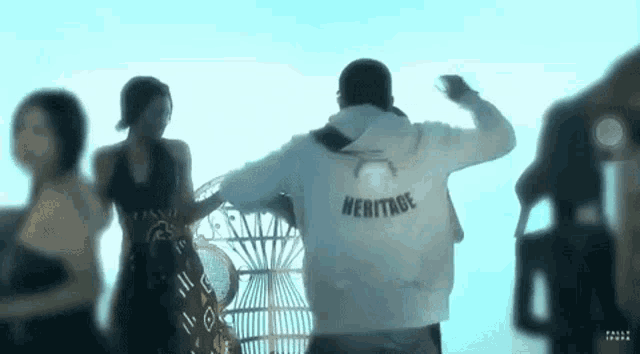 a man in a white hoodie with the word heritage on the back is standing next to a woman in a black dress .