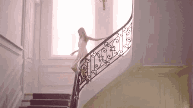a woman in a white dress is walking down a set of stairs with a wrought iron railing .