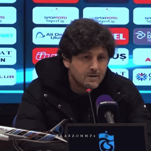 a man speaking into a microphone in front of a screen that says spor toto superlig