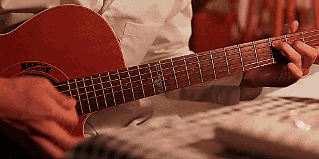 a man in a white shirt is playing an acoustic guitar with the letter l on the neck