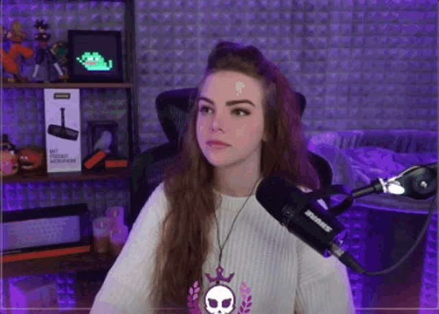 a woman wearing a white sweater with a skull on it is standing in front of a shure microphone