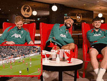 a man in a green aya shirt sits next to two other men in red chairs