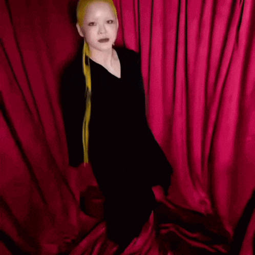 a woman with long blonde hair is standing in front of a red curtain with the words coco n on the bottom