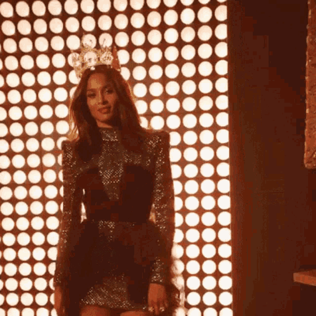 a woman wearing a crown is standing in front of a wall of circles