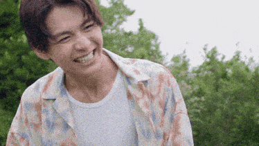 a young man wearing a floral shirt is smiling outdoors