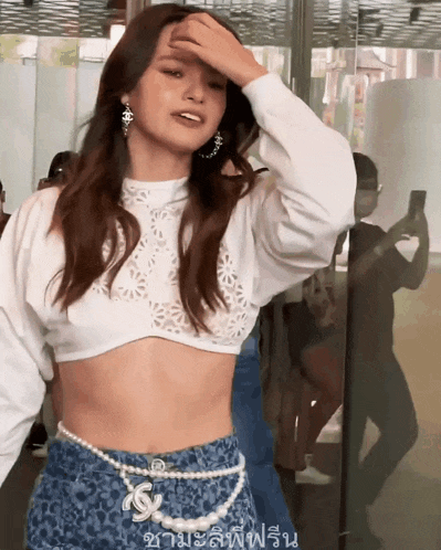 a woman wearing a white crop top and blue shorts with a pearl belt