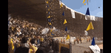 a crowd of people in a stadium with yellow and blue flags hanging
