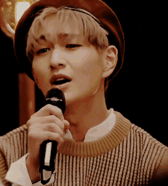 a man singing into a microphone with a hat on
