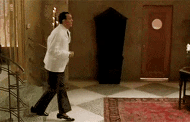a man in a white coat is walking in a room with a checkered floor .