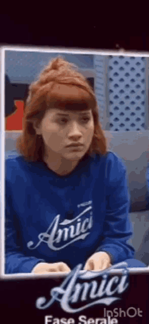 a woman with red hair is wearing a blue sweater and sitting on a couch .