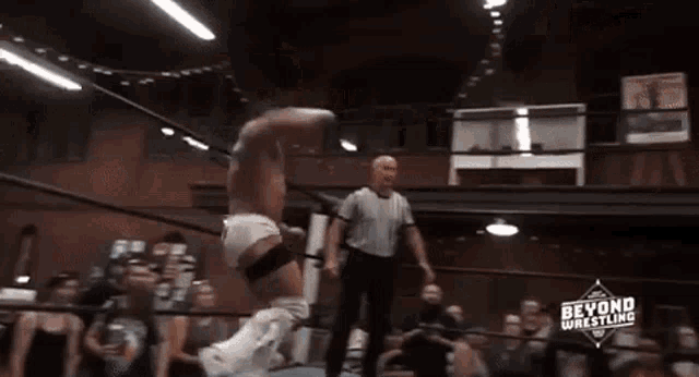 a wrestler is jumping in the air while a referee watches .