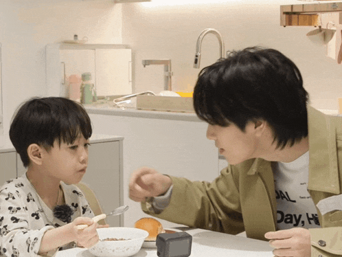 a man and a boy are sitting at a table eating cereal and the boy is wearing a shirt that says day