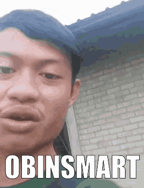 a man is making a funny face in front of a brick building with the words obinsmart written on the bottom .