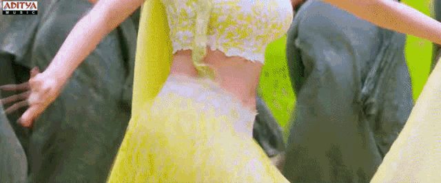 a woman in a yellow dress is dancing in front of a sign that says ' aditya ' on it