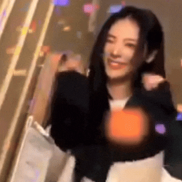 a woman is dancing in a room with a blurred background and a glowing heart in her hand .