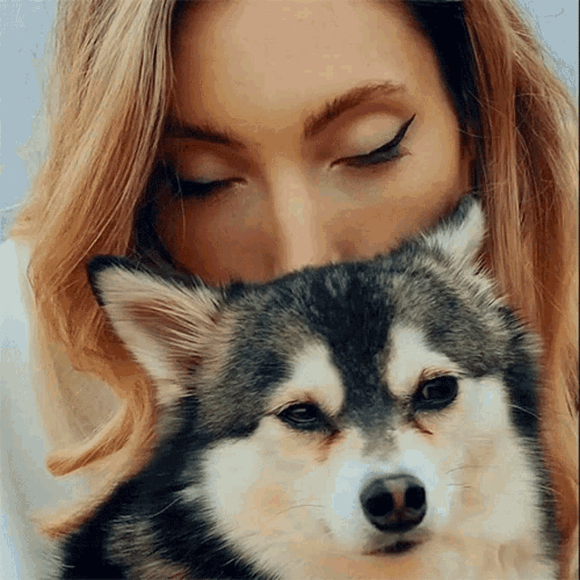 a woman with her eyes closed holds a husky puppy