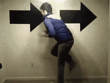 a man is standing in front of a wall with two large arrows pointing in opposite directions .