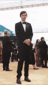 a man in a tuxedo is standing on a red carpet with his hands folded