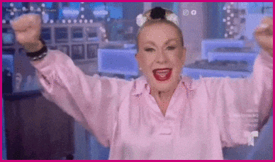 a woman in a pink shirt is raising her arms in the air and smiling .