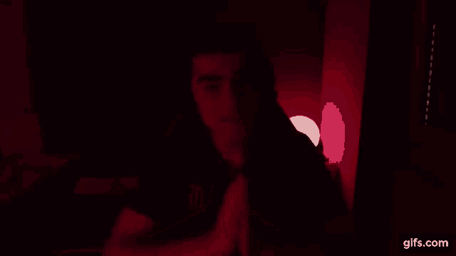 a man is sitting in a dark room with his hands folded in prayer .