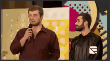 two men are standing next to each other and one of them is holding a microphone .