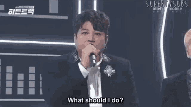 a man in a suit is singing into a microphone while another man looks on .