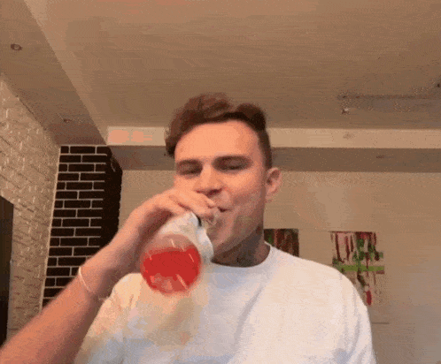 a man is drinking a red liquid from a bottle