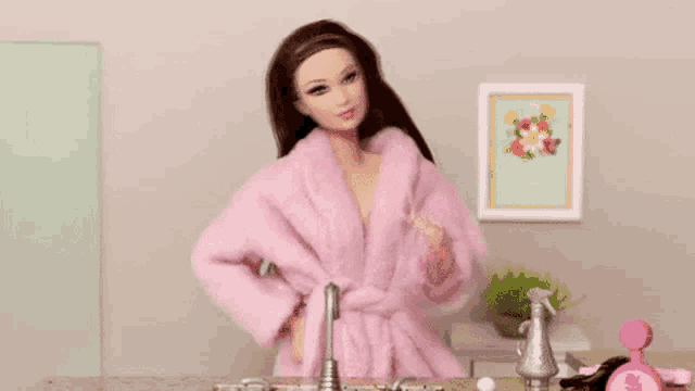 a barbie doll wearing a pink robe is standing in front of a bathroom sink .