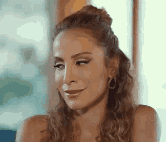 a woman with curly hair and hoop earrings is smiling and looking away from the camera .