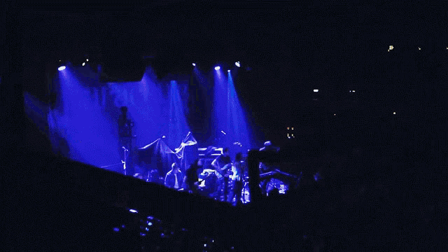 a group of people playing guitars and singing on a stage with a green exit sign in the background