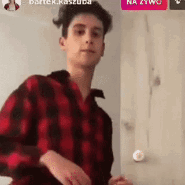 a young man wearing a red and black plaid shirt is standing in front of a white wall .
