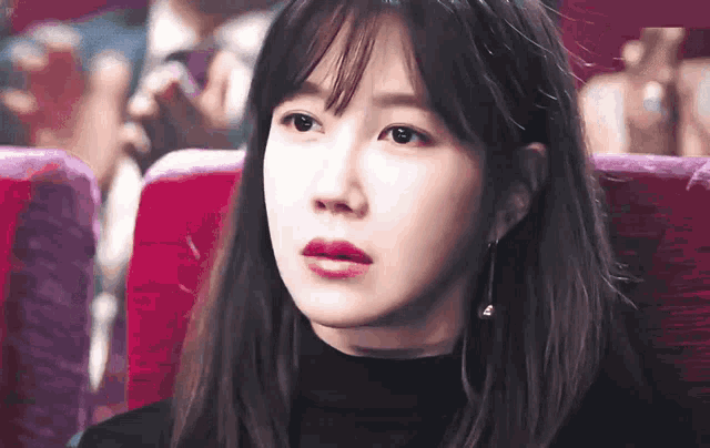 a woman in a black turtleneck is sitting in a red chair and looking at the camera
