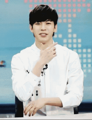 a young man wearing a white shirt is sitting at a table with his hands folded