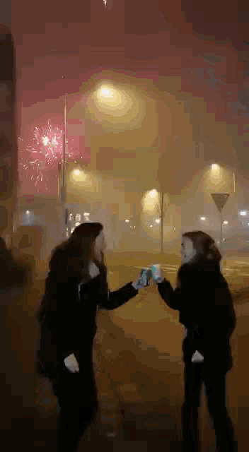 two women are toasting each other in front of fireworks
