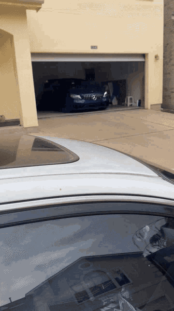 a white car is parked in front of a yellow house with a blue car parked in the garage