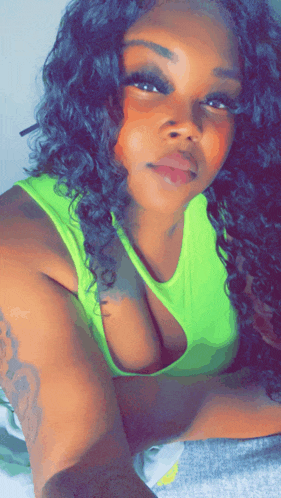 a woman in a neon green tank top is laying on a bed