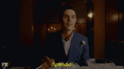 a man in a suit and tie says splendid in a dark room