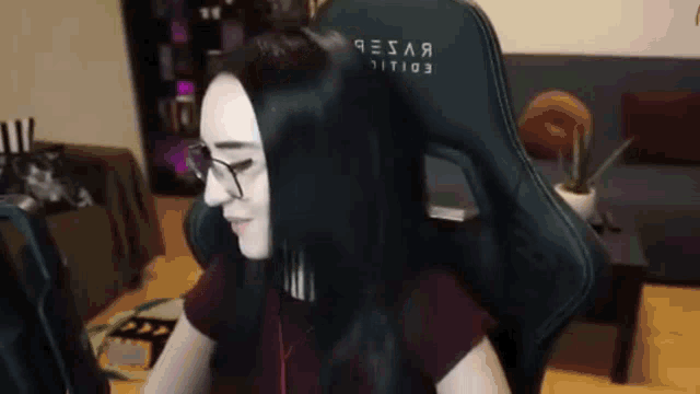 a woman wearing glasses is sitting in a gaming chair in front of a computer .