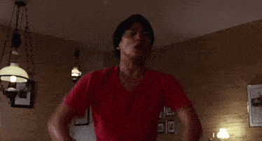 a man in a red shirt is standing in a room with a lamp hanging from the ceiling