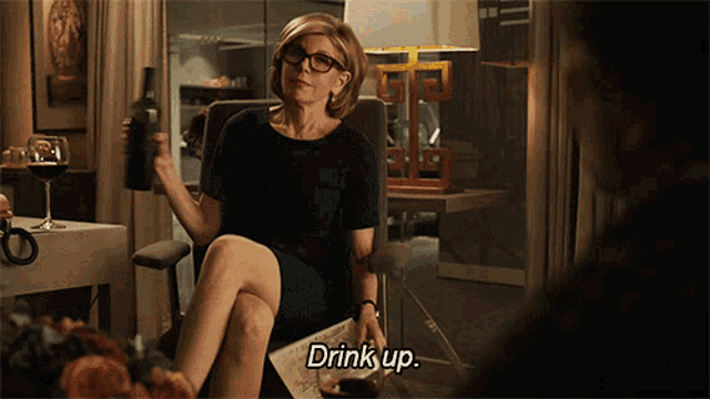 a woman is sitting in a chair holding a bottle of wine and the words drink up next to her