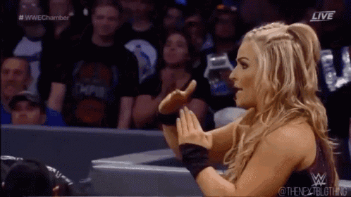 a female wrestler is standing in front of a crowd and making a funny face .