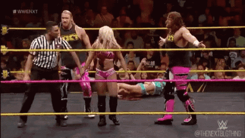 a group of wrestlers are standing around a woman in a ring .