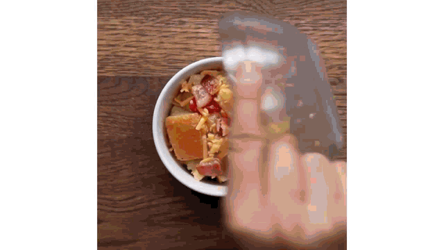 a person is pouring liquid into a bowl of food on a table .