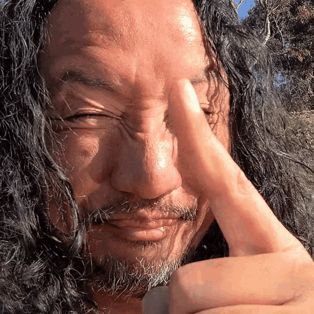 a man with long hair and a beard covering his eyes with his hand