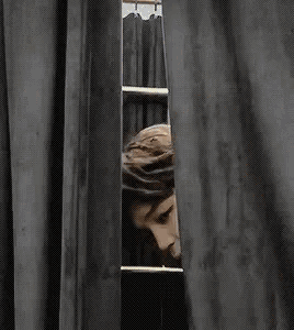 a person is peeking through a black curtain .